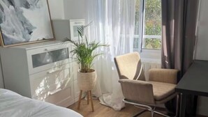 Une chambre à coucher moderne avec un lit, un bureau, une chaise, une plante en pot et une fenêtre avec des rideaux.