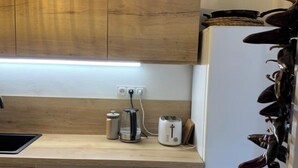 Une cuisine moderne avec des meubles en bois, un lave-vaisselle, un réfrigérateur, une bouilloire, un grille-pain et une plante suspendue.