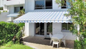 Une maison avec un patio couvert, une table et des chaises blanches, et une allée gravillonnée.