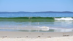Une plage avec une eau d’un bleu limpide, des vagues et des montagnes qui se dessinent à l’horizon.