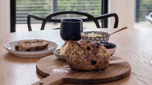 Une table en bois sur laquelle on trouve un pain, un bol de baies et une assiette avec une tranche de pain.