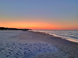Ein Strand mit Fußspuren, einem Steg und einem Sonnenuntergang.