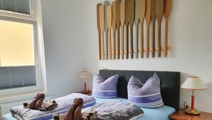 En snyggt bäddad säng med randiga sängkläder och två kuddar, ett sängbord med en lampa och en vägg dekorerad med träpaddlar.