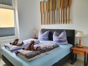 A neatly made bed with striped bedding and two pillows, a bedside table with a lamp, and a wall with wooden paddles.