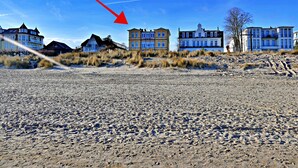 En fastighet vid stranden med flera byggnader, inklusive ett stort hus med en framträdande balkong och en mindre byggnad.