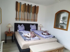 Ein Schlafzimmer mit einem Bett, zwei Nachttischen, einer Bank, einer Wanddekoration aus Holzruderern und einem dekorativen Spiegel.
