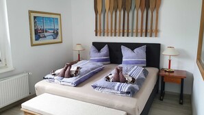 Un dormitorio con dos camas, un cabecero de madera con paletas, un cuadro en la pared y una ventana con vista a la playa.