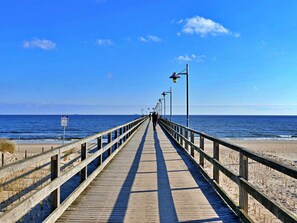 Ein hölzerner Steg erstreckt sich zum Meer, der Himmel ist wolkenlos.
