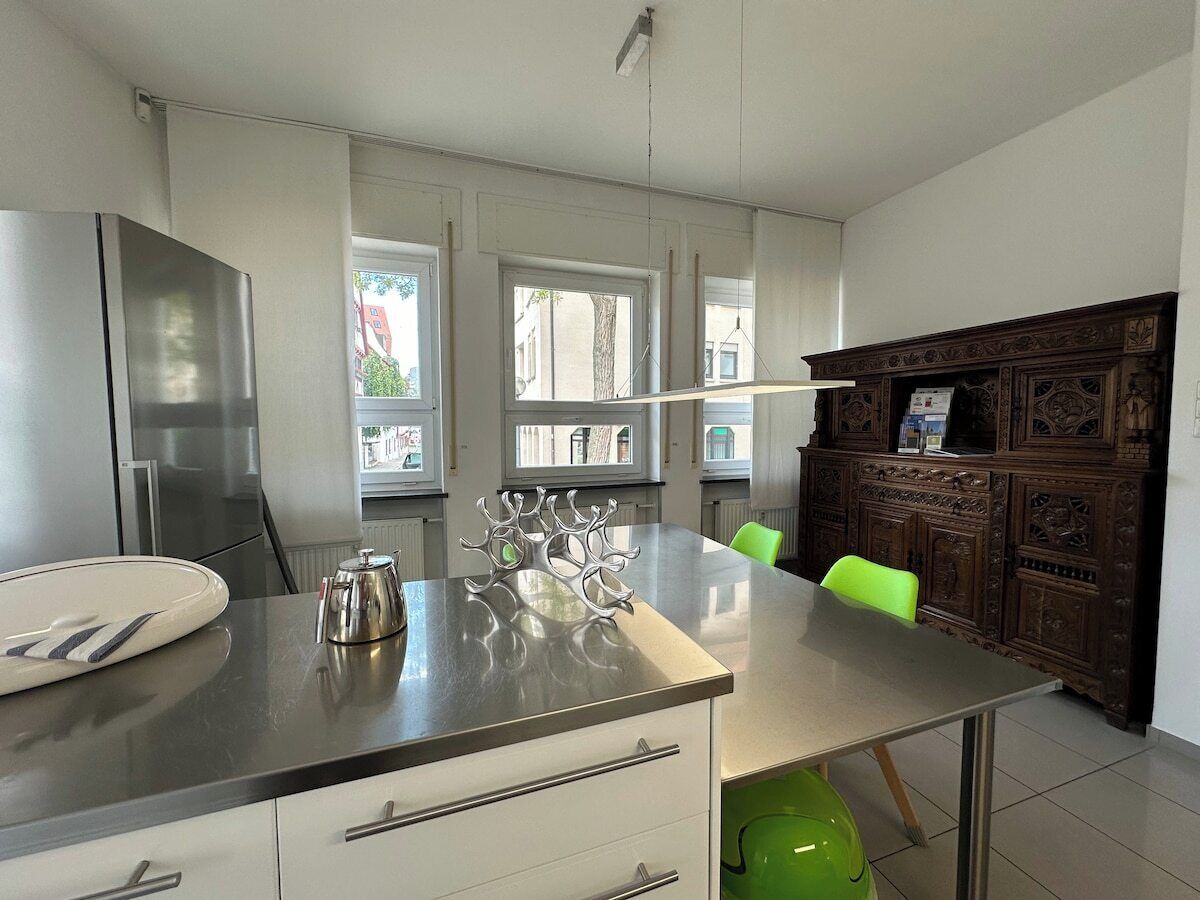 Una cocina moderna con una isla de acero inoxidable, armarios blancos y una silla verde.