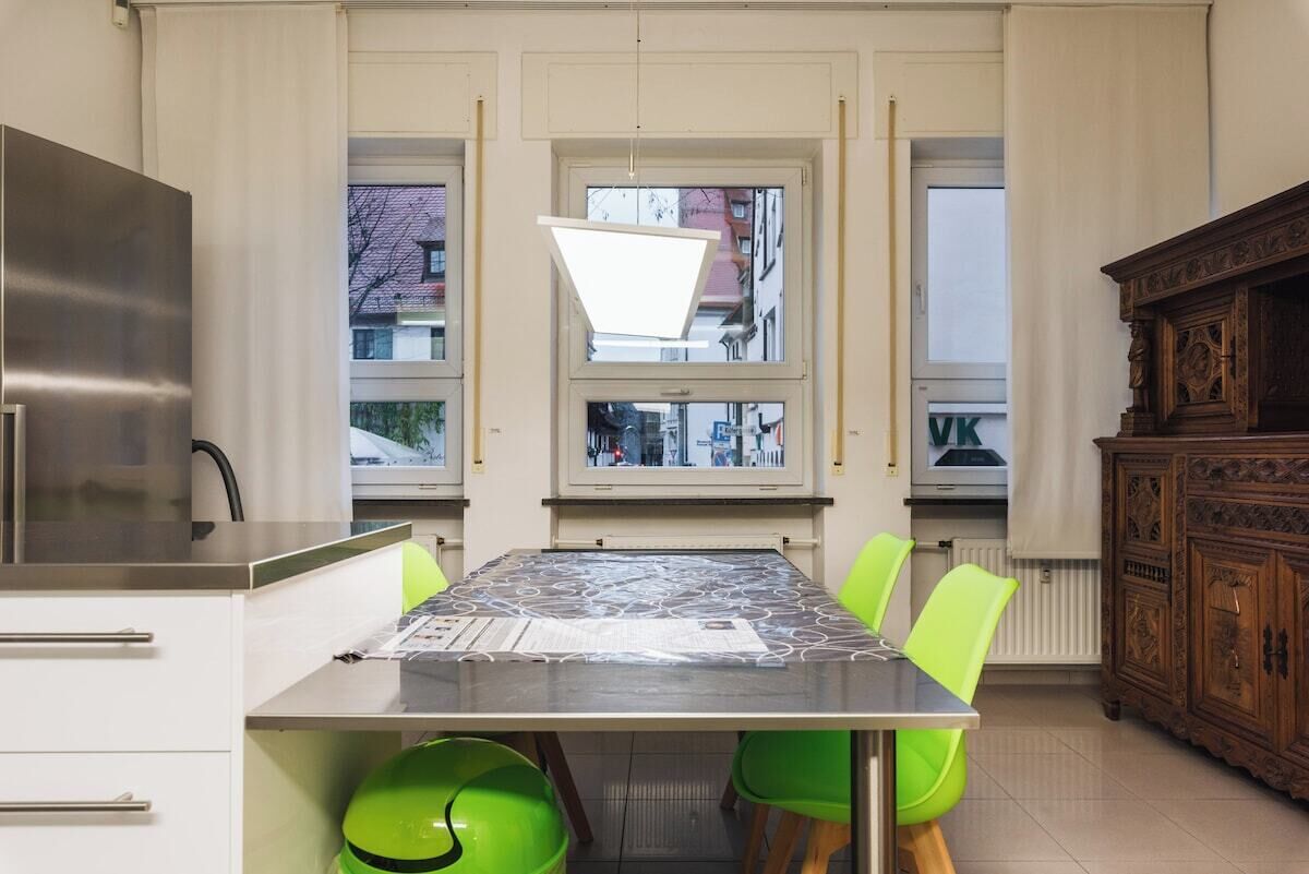 Een keuken met een eettafel, stoelen, een hanglamp en uitzicht door de ramen.