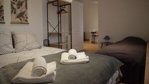 Quarto com cama, poltrona, mesa e planta pendurada.