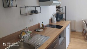 Et moderne køkken med en træbordplade, en indbygget vask og en kaffemaskine. Der er hylder over bordet med køkkenudstyr.