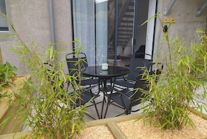 Une terrasse fermée par des parois de verre, avec une table ronde et quatre chaises, entourée de plantes de bambou.