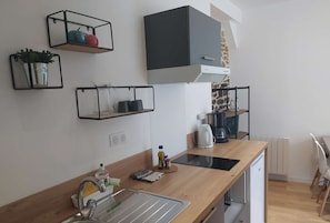 Une cuisine moderne avec un plan de travail en bois, un évier encastré et une machine à café. Des étagères au-dessus du plan de travail servent à ranger les ustensiles de cuisine.