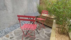 A patio with a stone floor, a small round table, and two red chairs. - Poterne du Tricot - Studio - 20m² - Maximum 2 Personnes (Guérande)