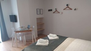 A neatly arranged bedroom with a bed, a desk, and a chair. There are towels on the bed and a small shelf unit against the wall. - Poterne du Tricot - Studio - 20m² - Maximum 2 Personnes (Guérande)