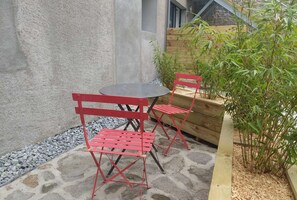 Un patio con piso de piedra, una pequeña mesa redonda y dos sillas rojas.