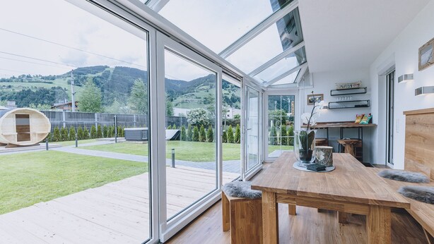 Una cocina moderna con una mesa de madera, vista a un jardín verde y una estructura de barril de madera en el exterior.