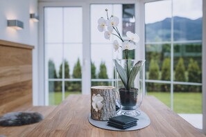 A wooden table with a glass vase containing white orchids, a wooden sculpture, and a black wallet on a woven mat. - Spa Chalet Lodges by we rent (Zell am See)