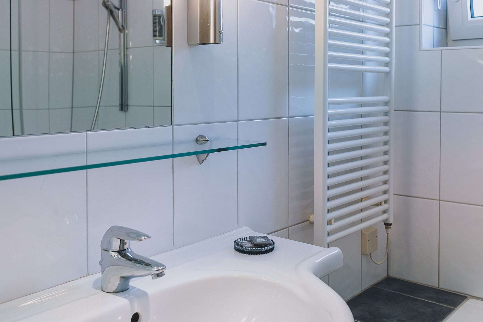 A bathroom with a white sink, a glass shelf, and a towel rack.