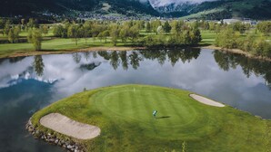 Un campo de golf con un estanque en primer plano y montañas al fondo.
