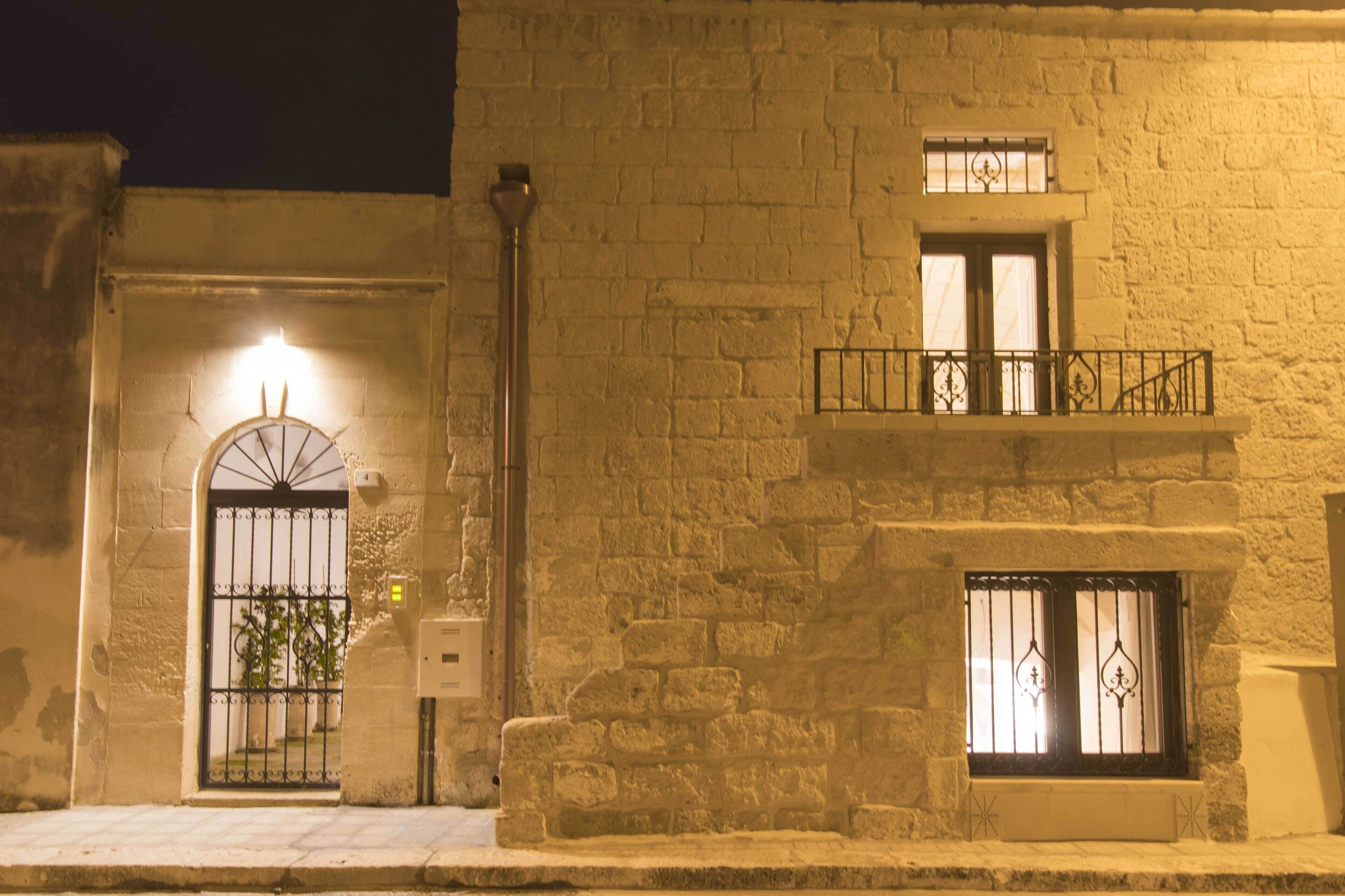 A stone building with a gated entrance, a balcony with metal railings, and a small window with decorative bars.