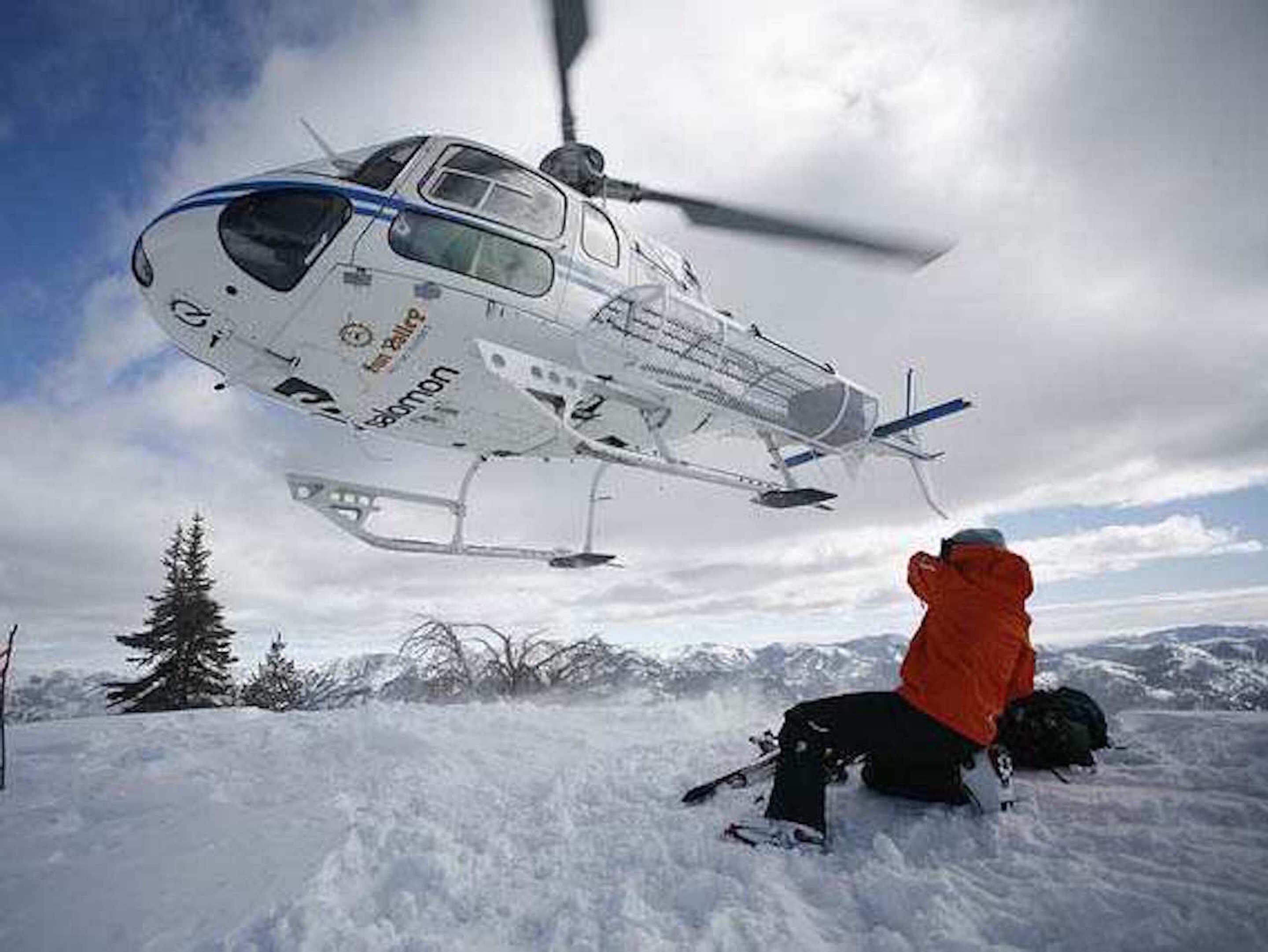 A person sitting on the snow with a helicopter flying overhead.