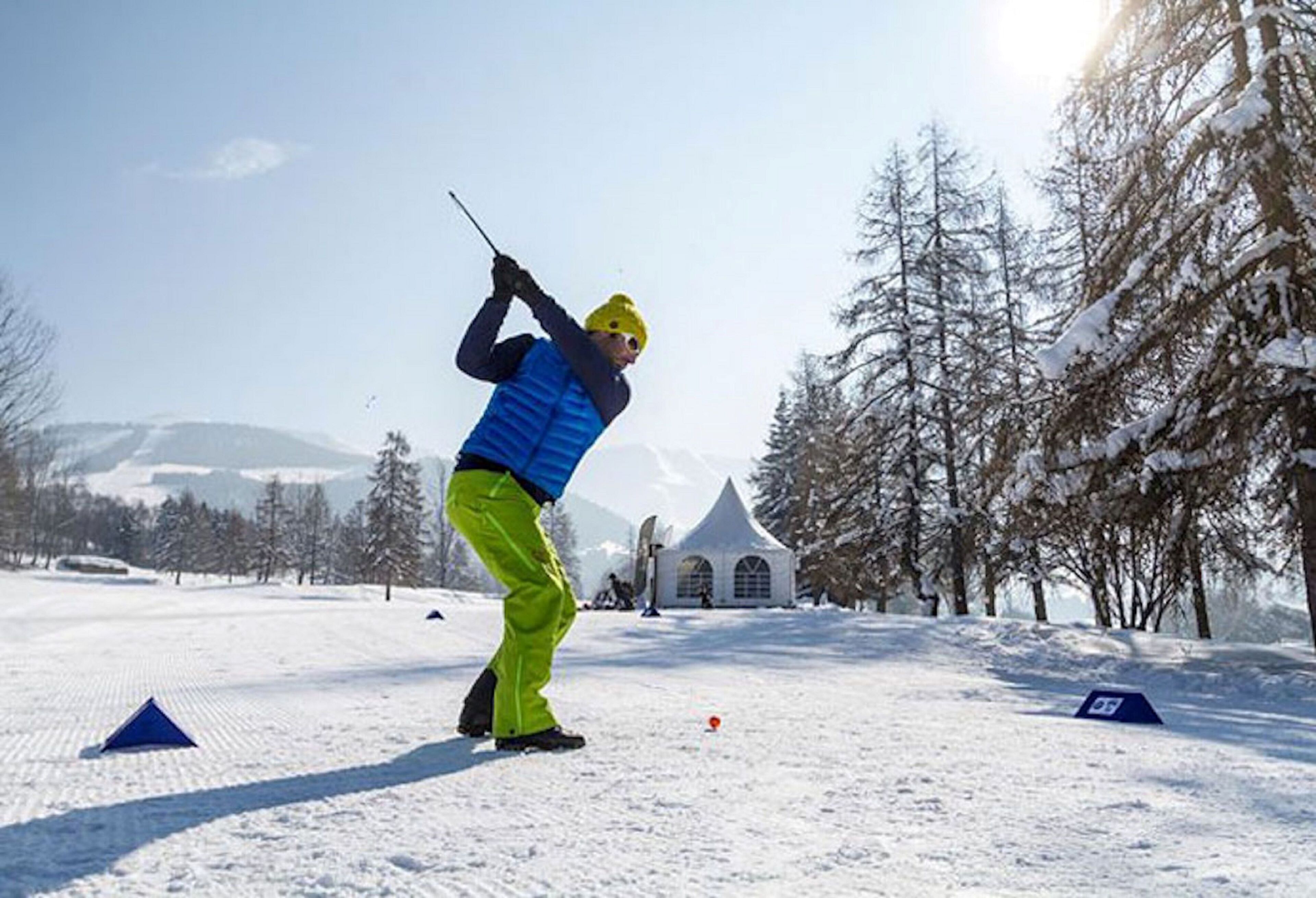 A person playing golf in a snowy outdoor setting with tents and trees in the background.