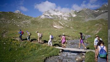 Eine Gruppe Wanderer überquert einen kleinen Bach über eine Brücke in einer gebirgigen Landschaft.