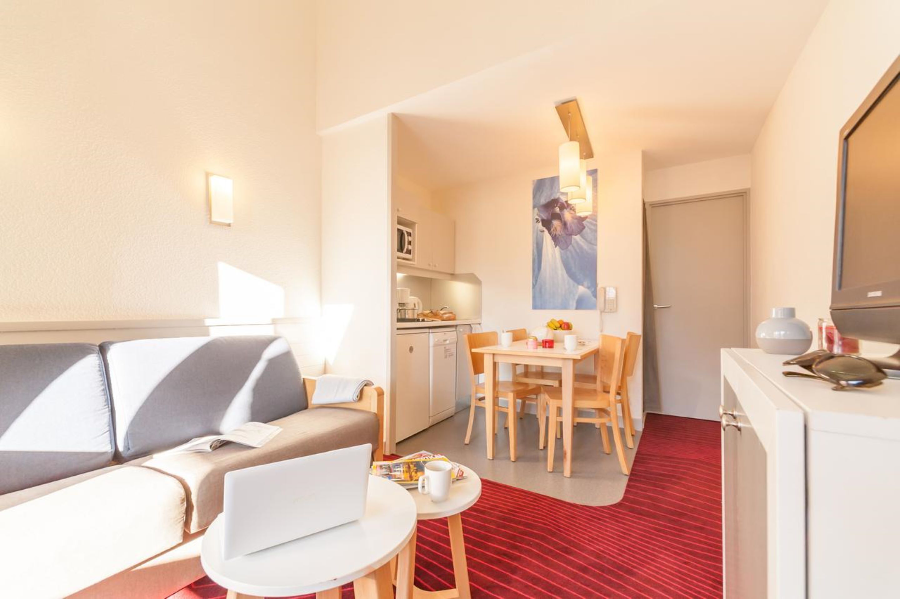 A compact hotel room with a sofa, a dining table, and a kitchenette.