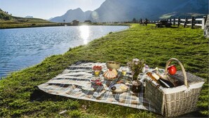 A picnic setup on a grassy area by a lake with mountains in the background. - Résidence La Daille - Val-d'Isère (Val-d'Isere)