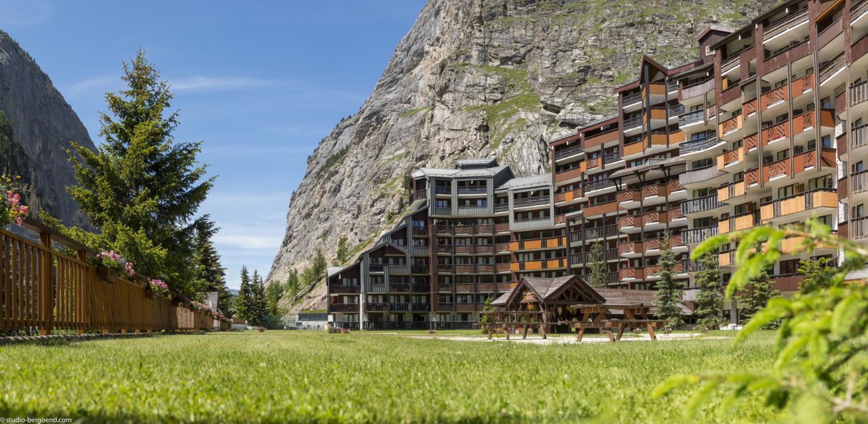 Un hôtel à plusieurs étages doté de balcons, avec une vue sur les montagnes et une pelouse bien entretenue.