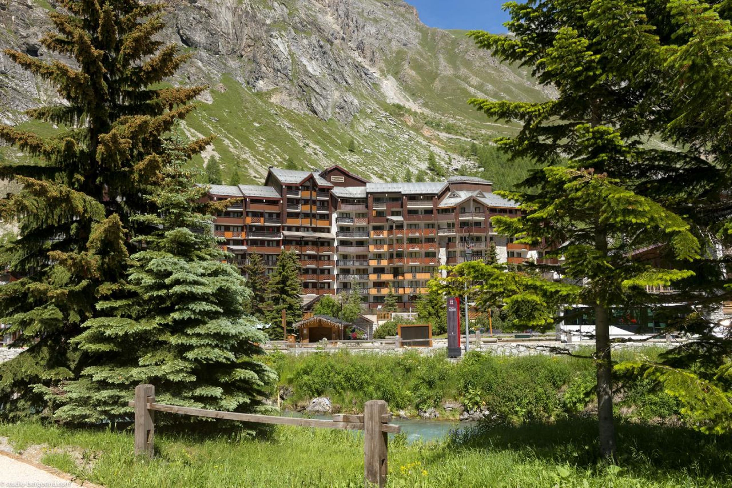 A multi-story hotel with balconies, set against a mountainous backdrop.
