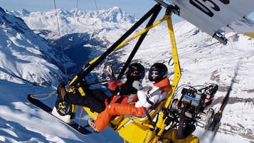 Une personne assise sur un télésiège jaune et noir, avec un paysage de montagne enneigé en arrière-plan.