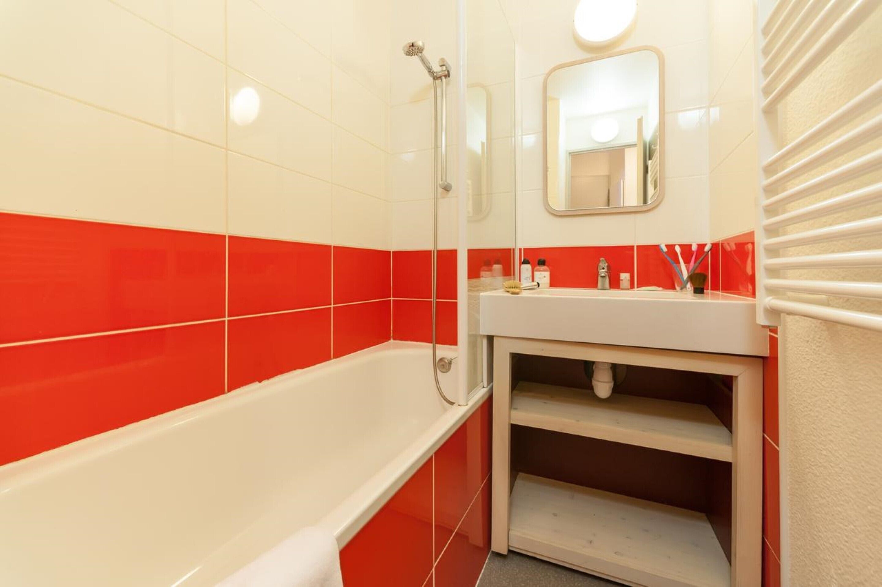 Une salle de bain avec une baignoire blanche, des murs carrelés de rouge et de blanc, un lavabo blanc et un miroir au-dessus du lavabo.