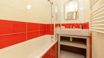 Ein Badezimmer mit einer weißen Badewanne, rot-weißen Fliesenwänden, einem weißen Waschbecken und einem Spiegel über dem Waschbecken.