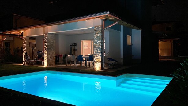 A modern house with a swimming pool, stone pillars, and a patio area with chairs and a table. - Villa Laura, with private heated pool and garden (Manerba del Garda)