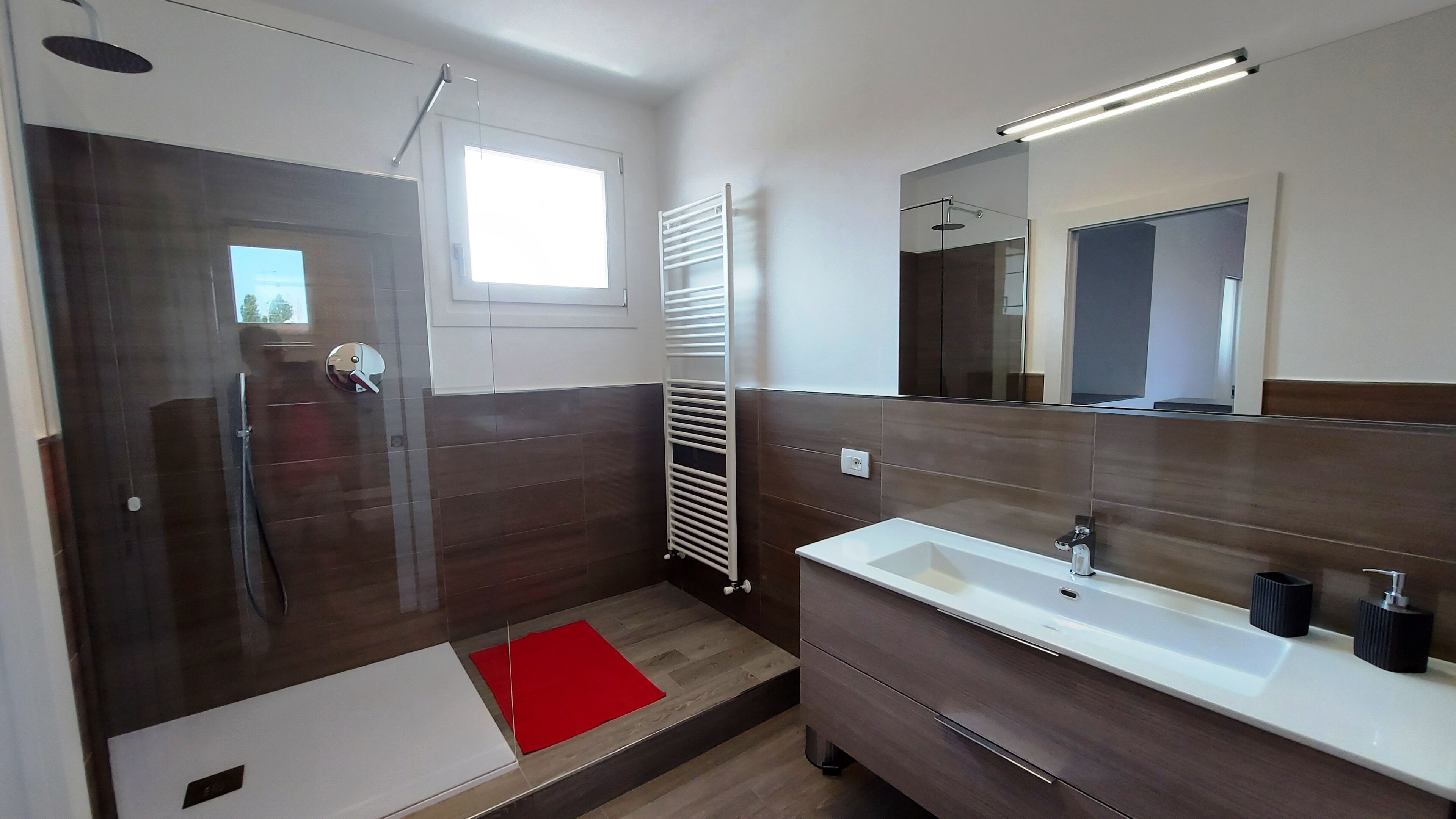Uma casa de banho moderna com chuveiro, um espelho grande e uma toucador com lavatório.