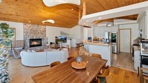 A spacious living area with a stone fireplace, wooden ceiling, and a large dining table.