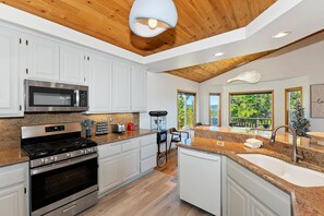 Una cocina moderna con gabinetes blancos, electrodomésticos de acero inoxidable y techo de madera.