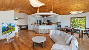A modern interior with a wooden ceiling, a kitchen area, a dining table, and a large window offering a view of greenery. - Breathtaking Views by Destination Big Bear : Extraordinary Lake Views in Ironwood Estates! Walk to the Village! Pool Table! (Big Bear Lake)