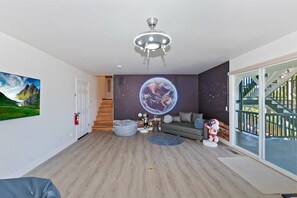 Una sala de estar moderna con un gran mural de la Tierra, un ventilador de techo, una escalera y vistas al exterior.