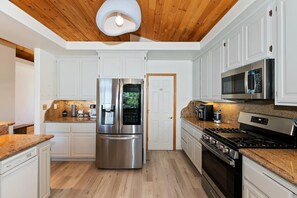 Une cuisine moderne avec des meubles blancs, des appareils en acier inoxydable et un plafond en bois.