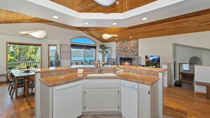 A spacious kitchen with a central island, wooden ceiling, and a stone fireplace.