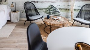 Ein modernes Schlafzimmer im Loft-Stil mit schräg versiegelter Decke, freiliegenden Backsteinwänden und einem Wandgemälde mit Fischen. Es gibt zwei schwarze Stühle, einen runden Holztisch und einen weißen runden Tisch.