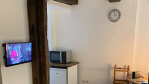 A room with a television, a microwave, a small refrigerator, a wooden chair, and a clock on the wall. - Historical Town Center Cosy Flat (Colmar)