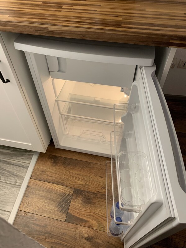 An open refrigerator with clear plastic shelves and a water dispenser.