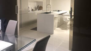 A modern kitchen with a central island, white cabinetry, and a glass dining table with chairs. - La Casa dei Gemelli (Priolo Gargallo)