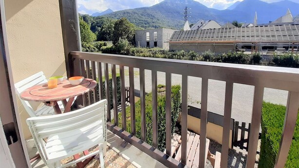 Een balkon met een tafel en stoelen, uitkijkend op een bergachtig landschap met gebouwen en een elektriciteitslijn.
