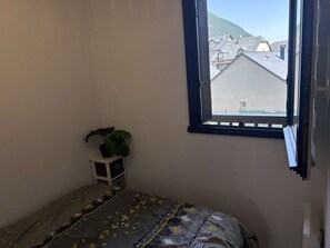 Une chambre à coucher avec un lit, une plante en pot et une fenêtre donnant sur des immeubles.